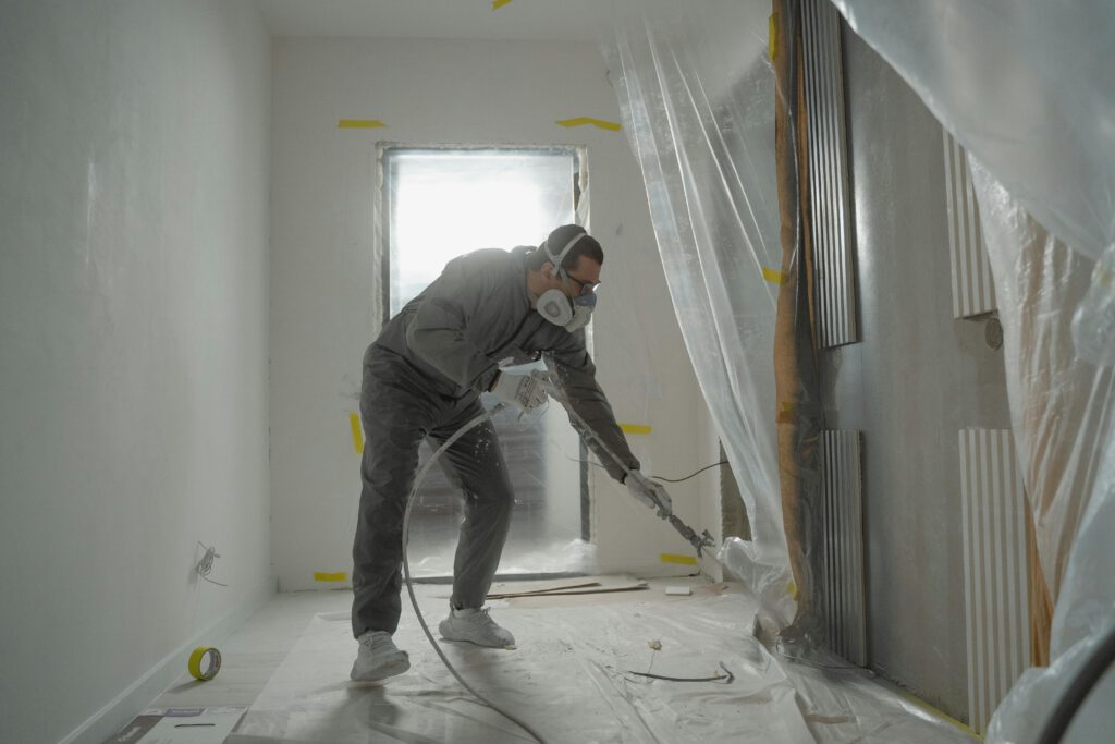 pexels-photo-6474300-6474300 A worker in protective gear painting walls during an indoor renovation project.